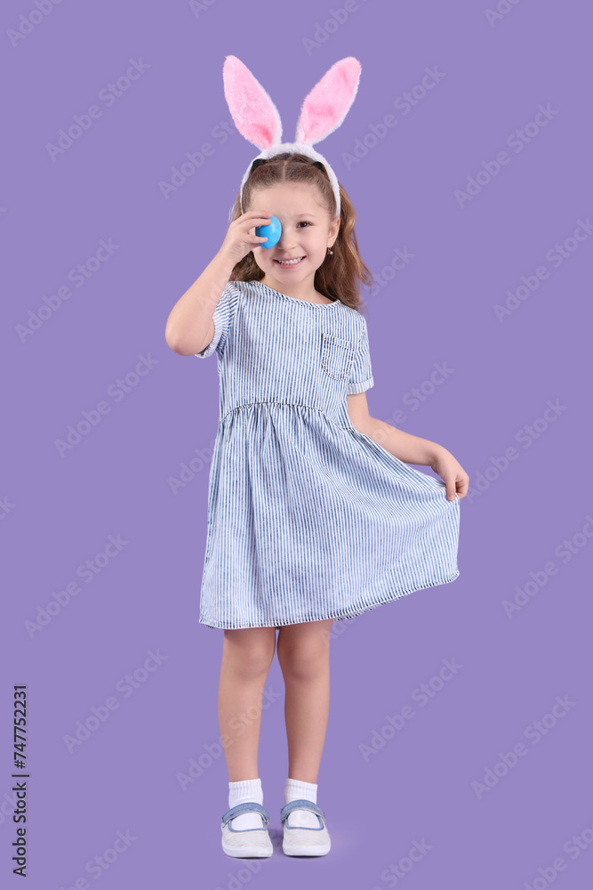 Cute little girl in bunny ears with Easter egg on purple background Cute little girl in bunny ears with Easter egg on purple background
