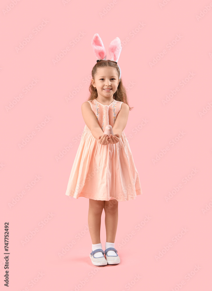 Cute little girl in bunny ears with bird on pink background. Easter celebration