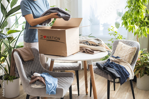 Donation concept. A woman collects clothes at home in a box for donation, recycling or disposal. photo