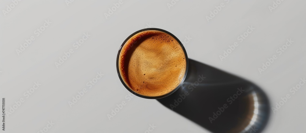 Fototapeta premium A black and brown cortado coffee cup is placed on a table with a gray background, casting strong shadows. The cup is the focal point of the composition, showcasing its sleek design and color contrast.