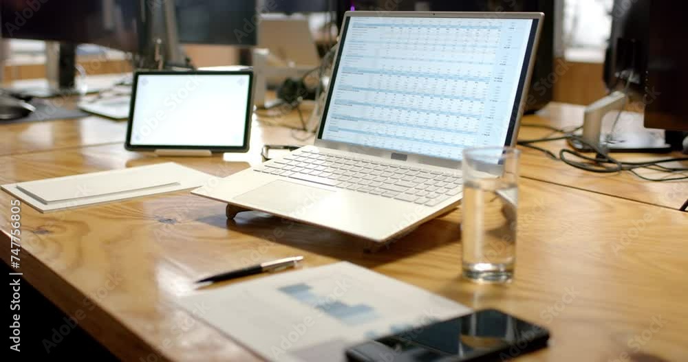 A modern business laptop open on a spreadsheet dominates a wooden office desk