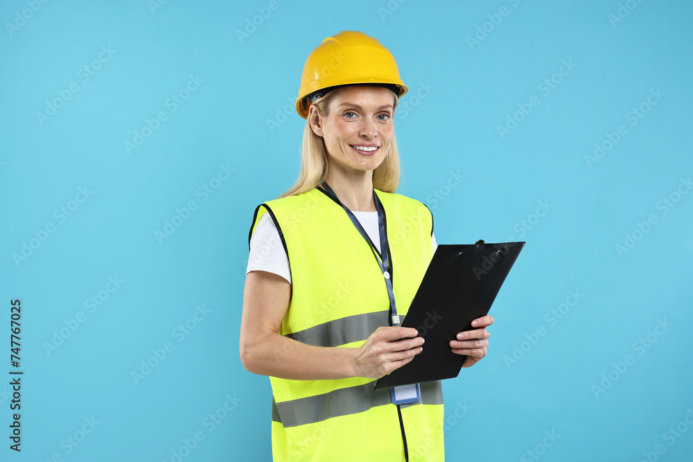Engineer in hard hat holding clipboard on light blue background Engineer in hard hat holding clipboard on light blue background