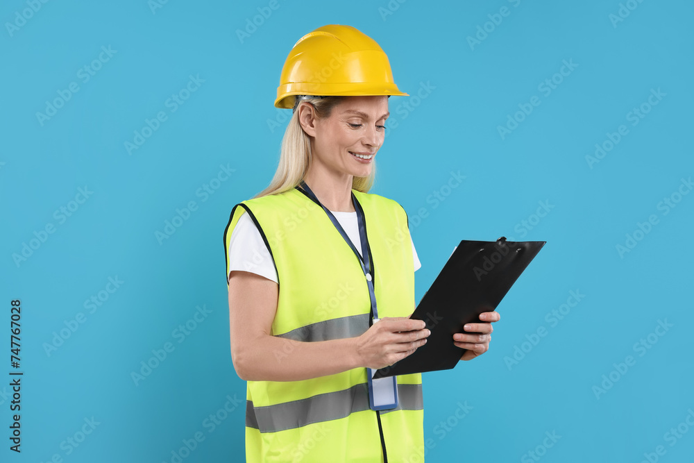 Engineer in hard hat holding clipboard on light blue background Engineer in hard hat holding clipboard on light blue background