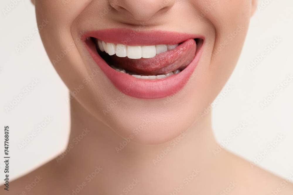 Obraz premium Young woman licking her teeth on white background, closeup