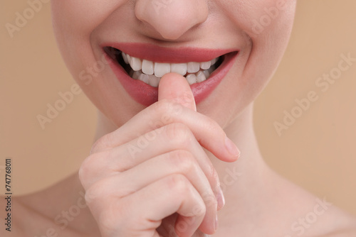 Young woman biting her finger on beige background, closeup