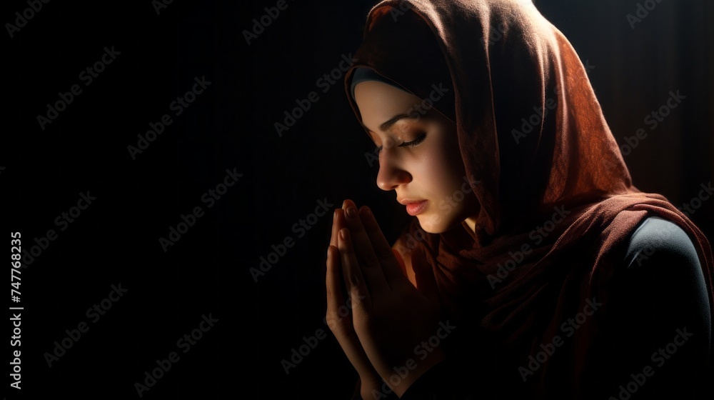 Obraz premium A beautiful young Muslim woman, wearing a traditional dress and hijab, Performs Divine services, Prays on a black background in a Mosque. Religion, Faith in God, Islam, Ramadan, Eid al-Adha concepts.