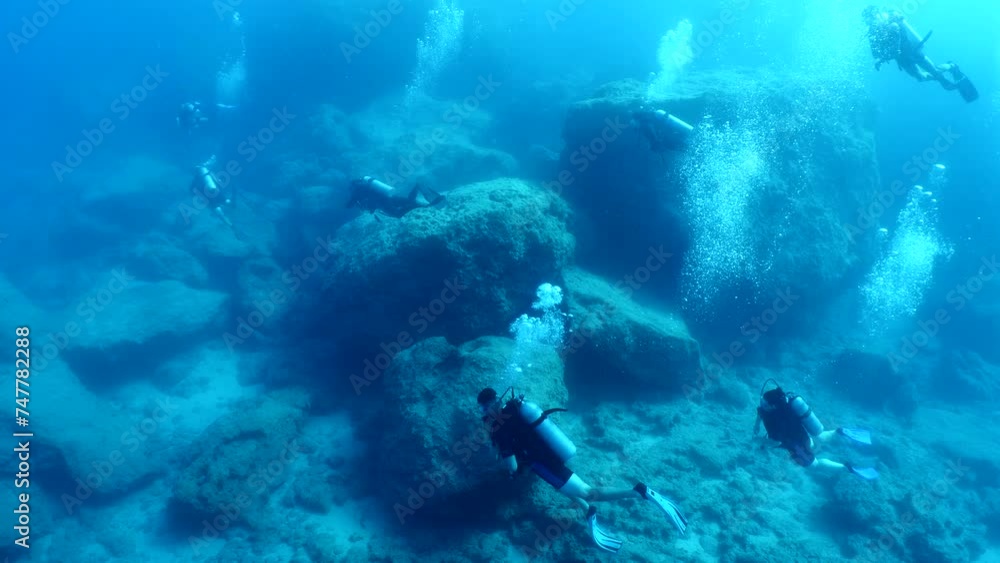 scuba divers exploring around a reef underwater deep blue water big rocks and bubbles ocean scenery 