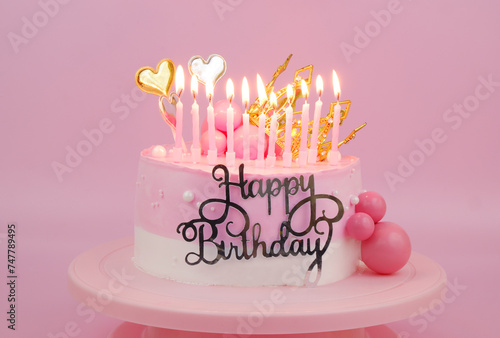 Birthday cake with many pink burning candles on pink background close up.