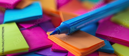 A blue pen is placed on top of a stack of assorted colored paper sheets, creating a vibrant and visually appealing display. The contrasting colors of the paper enhance the presence of the pen.