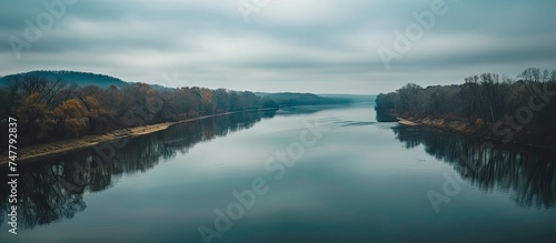 Aerial view of a river reflecting a cloudy sky, with dense trees bordering the waters edge creating a serene and lush landscape.