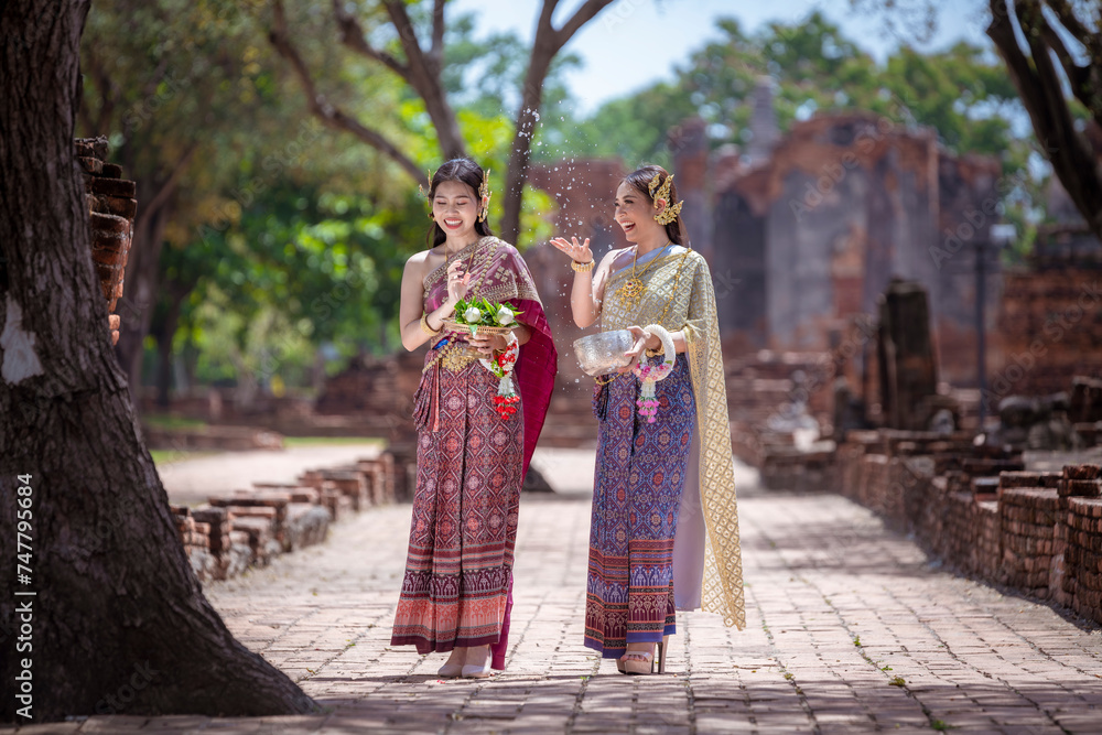 Beautiful Asian woman wearing Thai dress traditional pose happiness to playing splash water during Songkran festival is funny festival traditional holiday in Thailand .