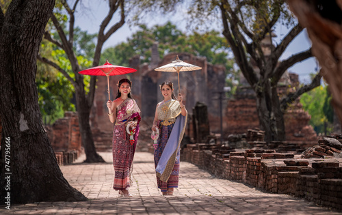 Asian beautiful wearing Thai traditional dress holding umbrella in ancient temple with old pagoda background. photo