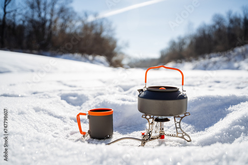 Camping equipment utensils stand on the snow while hiking against the background of the winter forest, kettle warming on the burner, boil water in winter conditions, trekking equipment