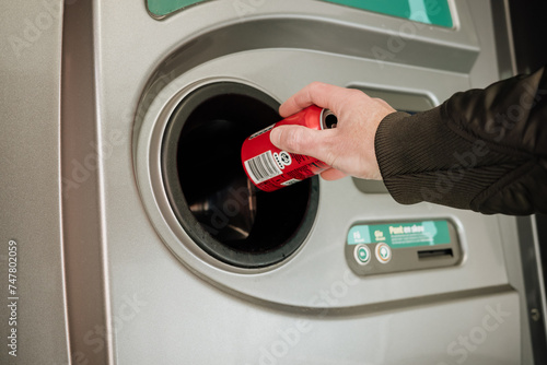 Returning empty bottles and cans in the recycling machine at the supermarket to reduce waste and reuse plastic, glass and aluminum. Hand holding a cola can in front of the machine.