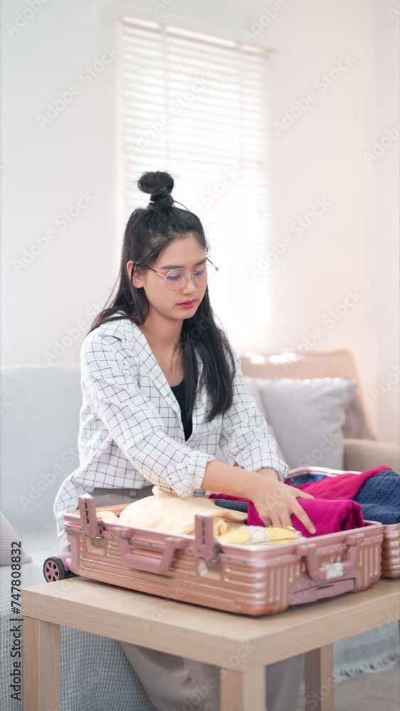 Asian woman efficiently rolls and packs clothes compactly, preparing to fit them into her travel bag Asian woman efficiently rolls and packs clothes compactly, preparing to fit them into her travel bag