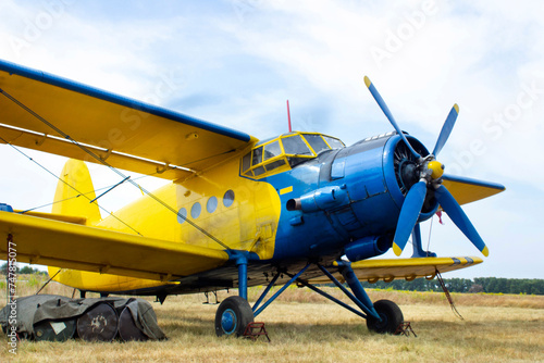Close-up of a small yellow-blue plane standing in a field. Old propeller plane close-up