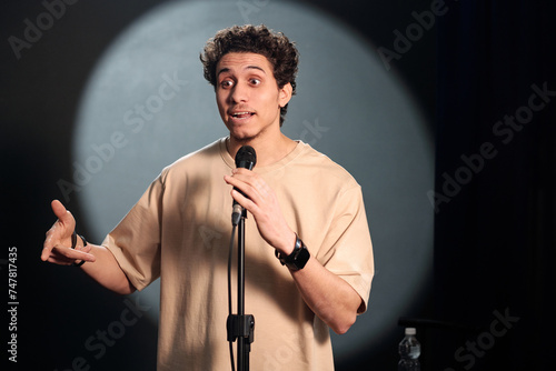 Quadro em tela Young comedian of stand up club standing on stage in front of audience and prono