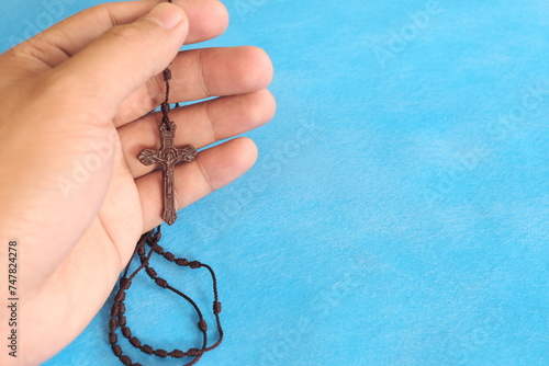 Male hands holding and praying the rosary or scapular in sky blue background.