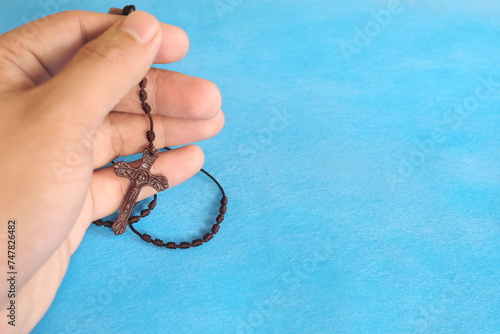 Male hands holding and praying the rosary or scapular in sky blue background. 