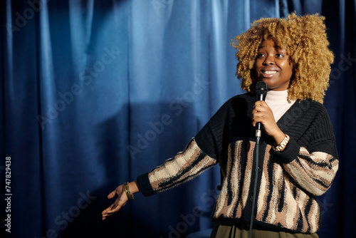 Εκτύπωση καμβά Young smiling female stand up comedian speaking in microphone during stage perfo