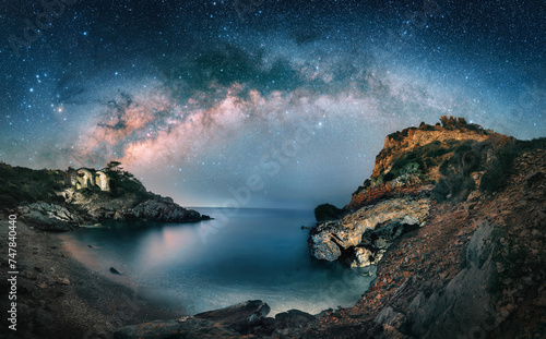 Amazing starry night sky with the majestic Milky Way over a scenic coast at a bay. A majestic landscape with cliffs and illuminated ruins © Smileus
