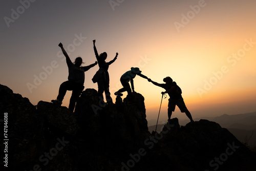Silhouette of Group team tourists lends helping hand climb cliffs mountains helping hand. teamwork people climbers climb top overcoming hardships, teamwork helping hand business travel concept.