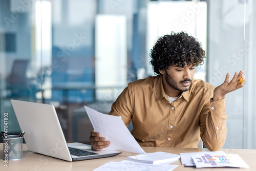 Tableau sur toile Clueless diverse male checking printed documents on desktop during working day in modern office interior