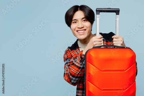 Traveler smiling happy man wear red casual clothes hold bag suitcase isolated on plain blue background studio. Tourist travel abroad in free spare time rest getaway. Air flight trip journey concept. #747852813
