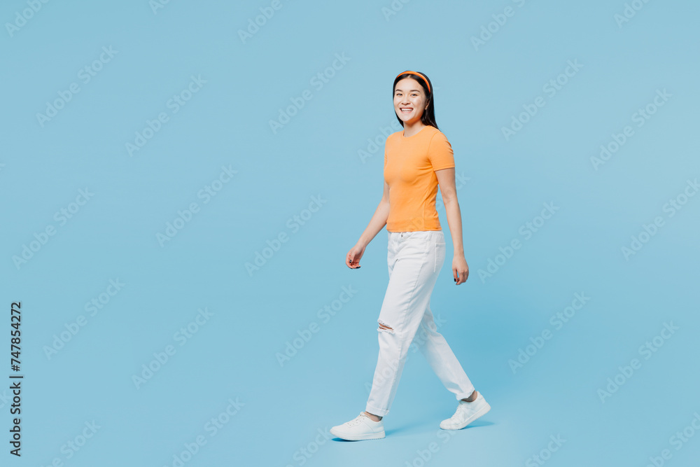 Full body side view smiling happy fun young woman of Asian ethnicity she wears orange t-shirt casual clothes walk go isolated on pastel light blue cyan background studio portrait. Lifestyle concept.. Full body side view smiling happy fun young woman of Asian ethnicity she wears orange t-shirt casual clothes walk go isolated on pastel light blue cyan background studio portrait. Lifestyle concept..