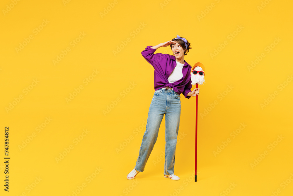 Full body young woman wear purple shirt casual clothes do housework tidy up hold in hand mop in hat and glasses look far away distance isolated on plain yellow background studio. Housekeeping concept. - obrazy, fototapety, plakaty 
