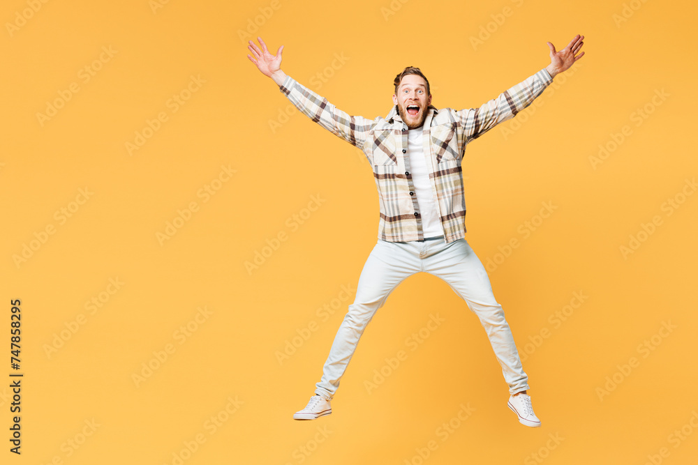 Full body overjoyed exultant young Caucasian man wear brown shirt casual clothes jump high with outstretched hands legs isolated on plain yellow orange background studio portrait. Lifestyle concept.