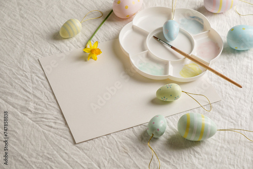 Easter, spring, copy space, Easter decorative eggs in pastel colors and narcissus on the table, white background, watercolor paints and palette, 