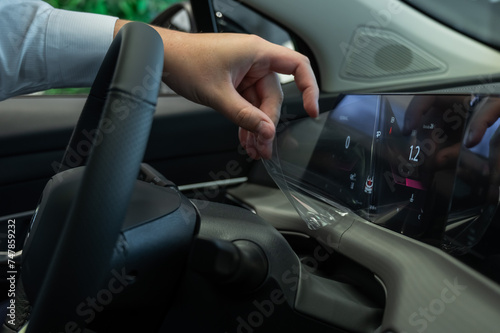 A man removes the protective film from the dashboard of a new car. 