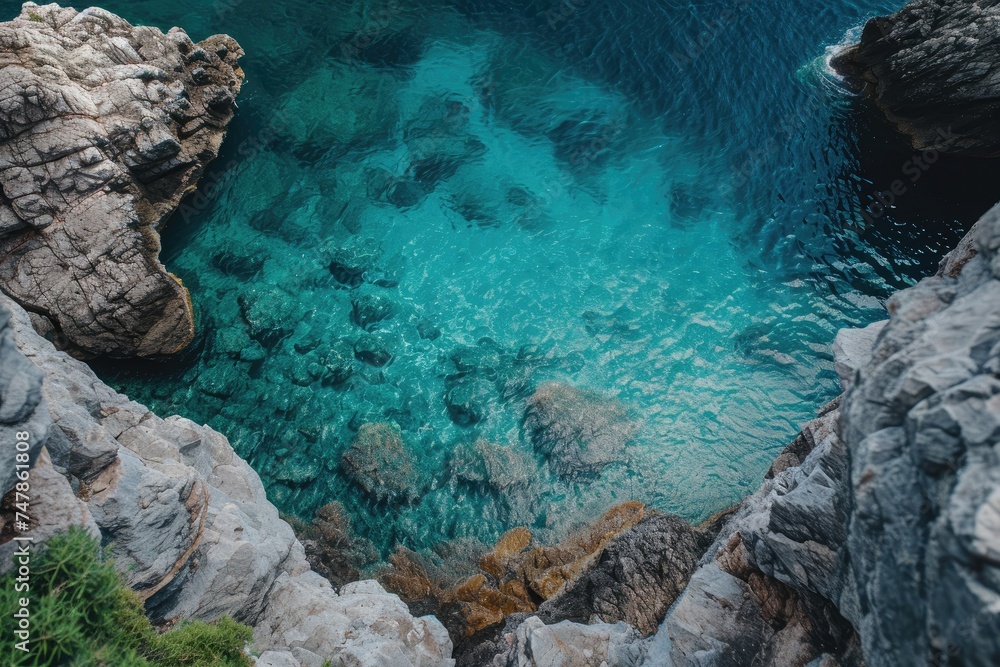 A body of water encircled by rugged rocks, creating a contrast between the clear blue water and the solid formations, Top view of a calm sea brushing against harsh rock faces, AI Generated
