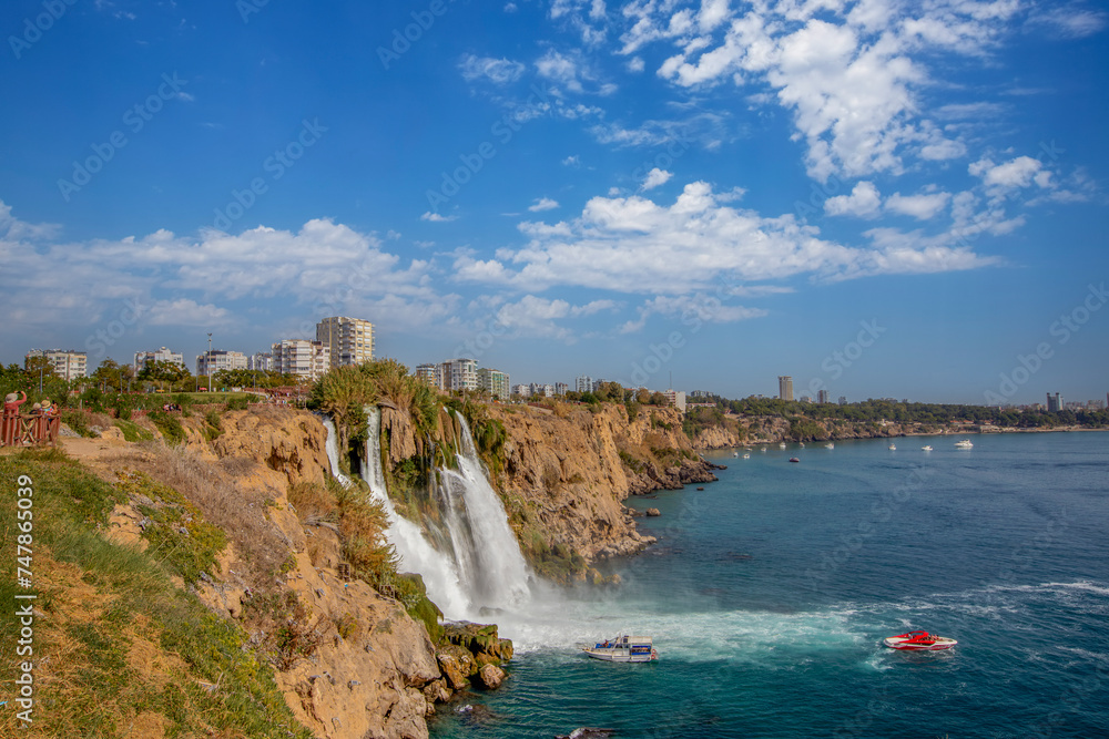 The moment when the Lower Düden waterfall flows into the sea, against the background of the steep shores of the Mediterranean and the urban development of the city of Antalya.