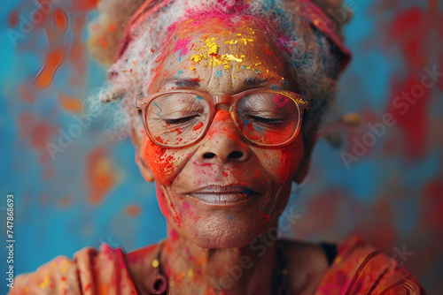 Background for Holi holiday, voluminous and airy colored powder on the face of an elderly old woman and empty space for design.