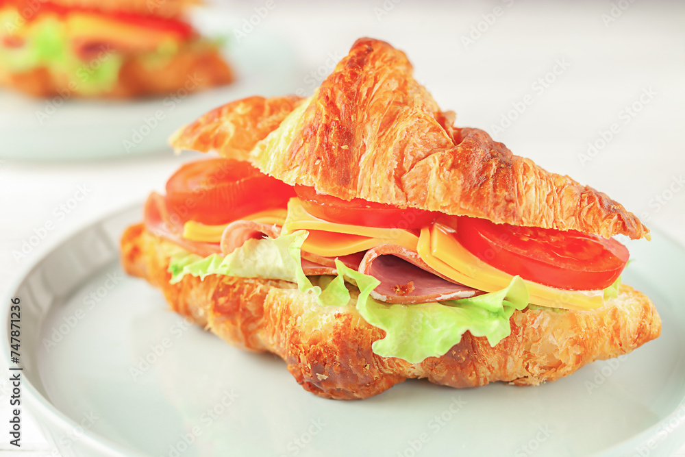 Fresh croissant with ham and lettuce on white wooden background