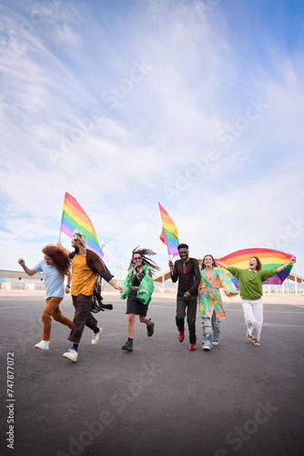Vertical of a group of LGBT people is leisurely walking down the street in the gay pride day parade holding colorful rainbow flags, enjoying a fun and happy event. Diverse men and women run together