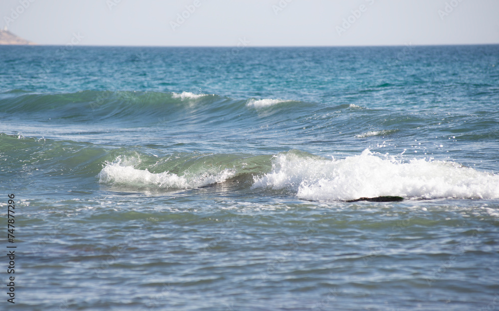 Small waves in the mediterranean sea, turquoise water, white foam, and a foggy horizon