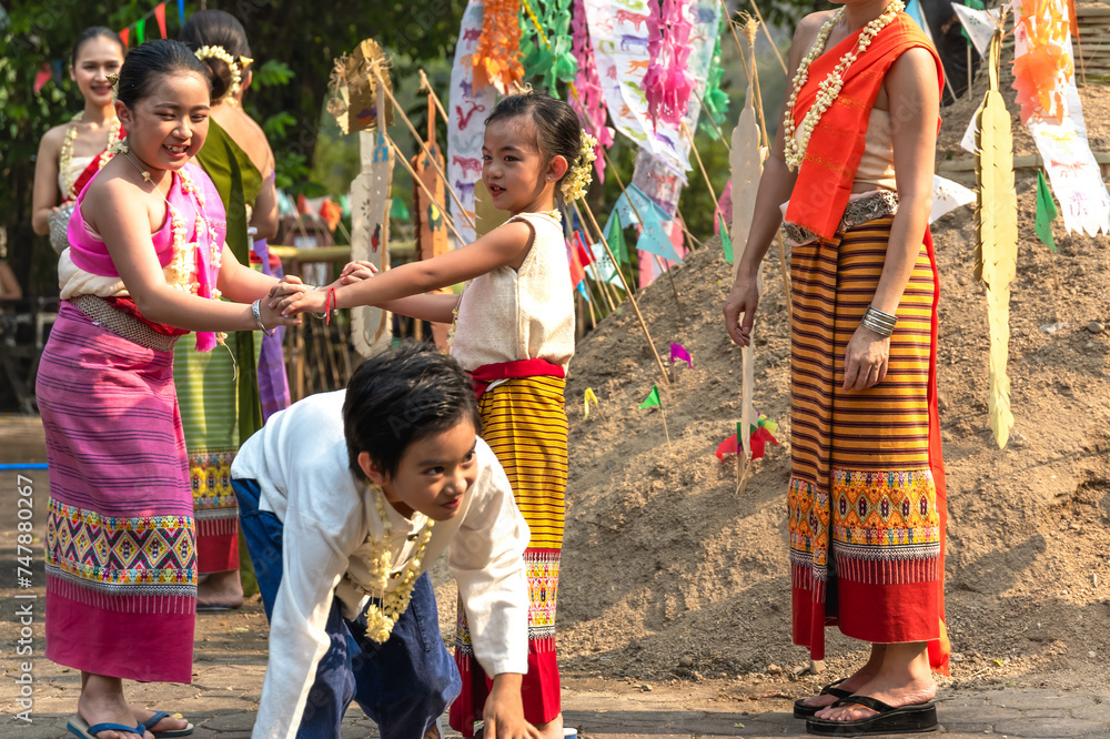 Naklejka premium Boy and girls in traditional Thai clothing playing together at sand castle during Song kran festival in Chiangmai, Thailand