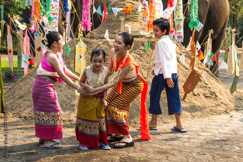 Thai boy and girls in traditional Thai dresses playing near sand castle decorating with colorful flags during Song Kran festival in chiangmai, Thailand 
