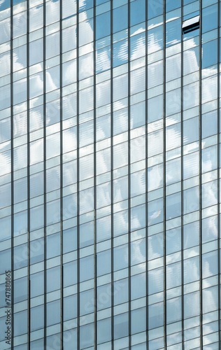 windows of modern office building exterior reflects cloudy sky.