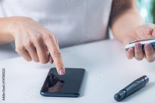 A woman tracks glucose levels and inputs data via smartphone, vital for diabetes management and health monitoring © Microgen