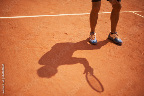 Tennis, court and shoes of athlete outdoor at start of exercise of workout in competition. Person, shadow and sneakers on feet of player training on clay pitch in game of sport with fitness or action © Katie/peopleimages.com
