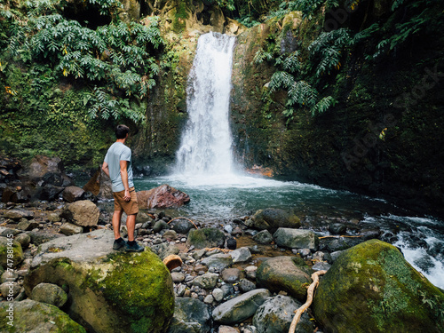 Young man (traveler) standing in Azores waterfall in tropical rainforest. Traveling for discovery. Peace in the heart. Spring leaves. Concept of tranquility.