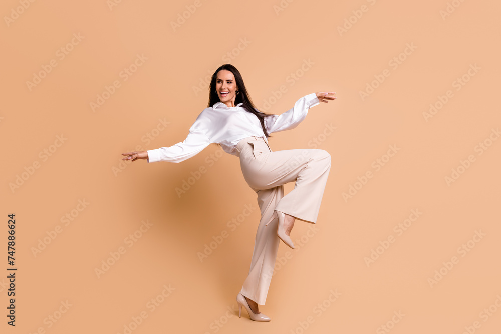 Full length photo of adorable pretty woman wear white shirt dancing having fun empty space isolated beige color background Full length photo of adorable pretty woman wear white shirt dancing having fun empty space isolated beige color background