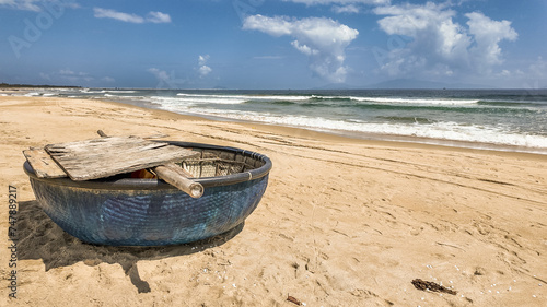 Traditional round Vietnamese fishing boat on a tranquil sandy beach with ocean waves and ample copy space in the sky, evoking a sense of peaceful seaside life