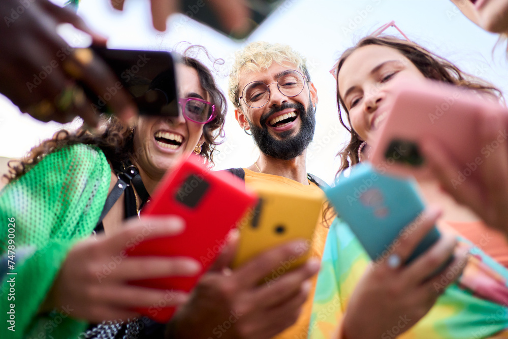 Obraz premium A group of happy people is celebrating and sharing a fun moment using mobile with their colorful cell phones, smiling and making gestures. Youth people o millennial generation addicted to technology