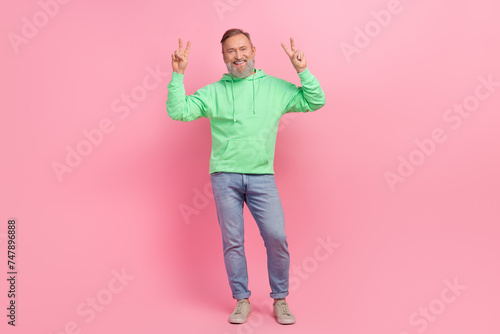 Full length photo of handsome senior man show double v-sign dressed stylish green garment isolated on pink color background © deagreez