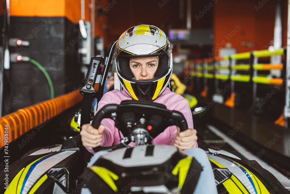female driver looking at camera defiantly with her racing helmet holding the steering wheel of the karting car at the starting line on the circuit female driver looking at camera defiantly with her racing helmet holding the steering wheel of the karting car at the starting line on the circuit